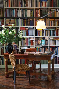 a room filled with lots of books and a table topped with a vase full of flowers