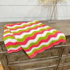 a crocheted blanket sitting on top of a dresser next to a vase with flowers