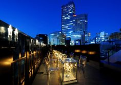 an outdoor dining area in front of a city skyline at night with lights on the tables