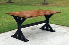 a wooden table sitting on top of a cement slab in front of some green grass