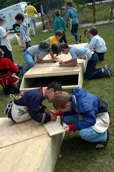 several children are sitting on wooden benches in the grass and one boy is writing something