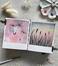 an open book sitting on top of a table next to flowers and paintbrushes