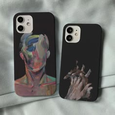 two iphone cases with paintings on them sitting on top of a white bed next to each other