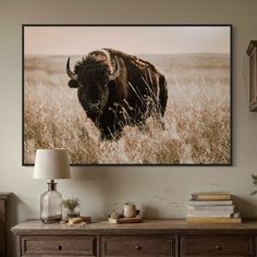 a bison standing in tall grass on a wall above a dresser with a lamp next to it