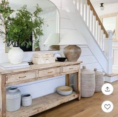 a wooden table sitting under a mirror next to a stair case and potted plant