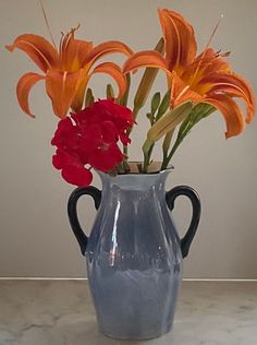 a blue vase with red and orange flowers in it on a white countertop next to a wall