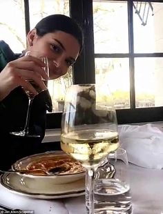 a woman sitting at a table with a glass of white wine in front of her