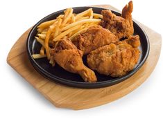 fried chicken and french fries on a black plate with a wooden serving board next to it