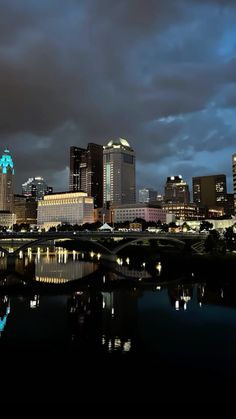 the city skyline is lit up at night with clouds in the sky and reflecting on the water