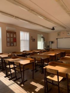 an empty classroom with wooden desks in the middle and a projector screen on the wall