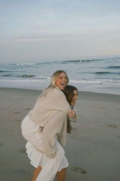 two women walking on the beach with their arms around each other's shoulders and laughing