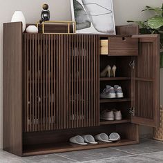 a wooden cabinet with shoes and pictures on the top shelf, next to a potted plant