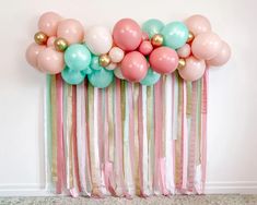 balloons and streamers are hanging on the wall behind a pink, green, and gold curtain