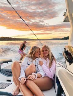 two women are sitting on the back of a boat at sunset while another woman watches