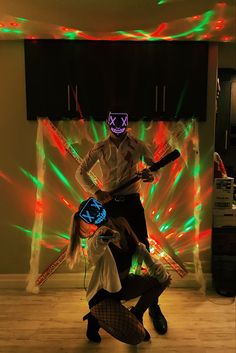 two people dressed up in costumes with lights on the wall and behind them, one person is holding a guitar