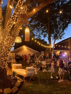 a group of people standing around a tree with lights hanging from it's branches