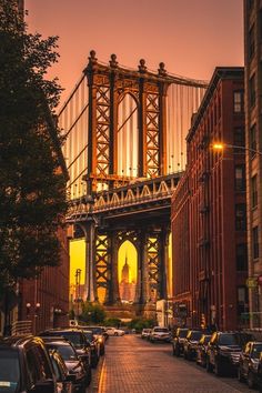 cars are parked on the side of the road in front of an old bridge at sunset