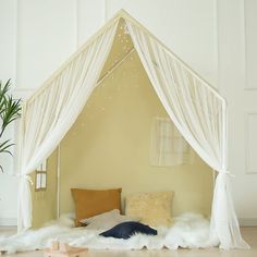 a bed with white drapes and pillows in a room next to a potted plant