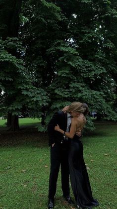 a man and woman in formal wear embracing each other on the grass with trees in the background