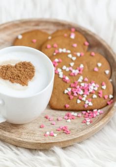 two heart shaped cookies on a plate next to a cup of hot chocolate and sprinkles