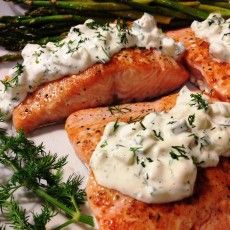 salmon and asparagus on a white plate with cream sauce, dill sprigs