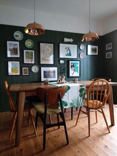 a dining room table with chairs and pictures on the wall behind it in green tones