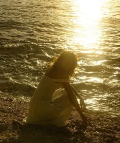 a woman kneeling on the beach at sunset