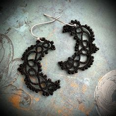 a pair of black lace earrings sitting on top of a gray surface with an intricate design