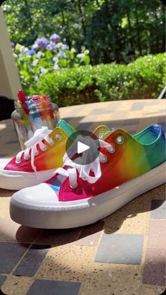 a pair of rainbow colored shoes sitting on top of a tiled floor next to flowers