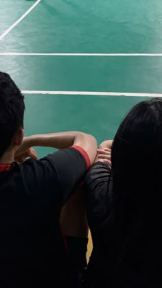 three people sitting on a bench looking at a tennis court with a ball in the air