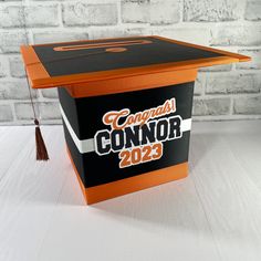 an orange and black box with the words congrats connor on it sitting in front of a brick wall