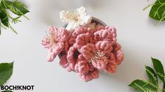 a bowl filled with pink and white crocheted flowers next to some green leaves