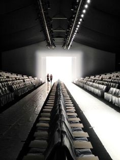 two people standing in the middle of an empty room with rows of chairs on either side