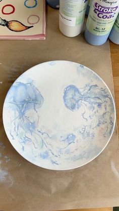 a white plate sitting on top of a wooden table next to paint bottles and glue