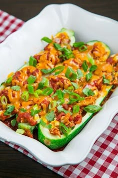 a casserole dish with zucchini, cheese and other toppings on a checkered table cloth