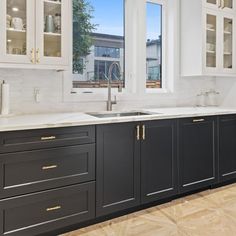 a kitchen with black cabinets and white counter tops in front of two large windows that look out onto the street