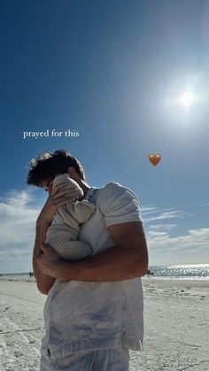 a man holding a baby while standing on top of a sandy beach