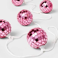 three pink disco ball ornaments with white string attached to each ornament on a white background