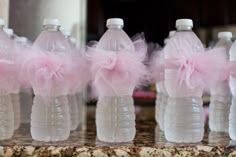 three plastic water bottles with pink tulle bows on them sitting on a marble counter