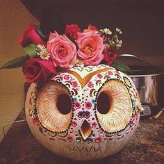 a decorated pumpkin with roses and an owl face on it's head, sitting on a counter