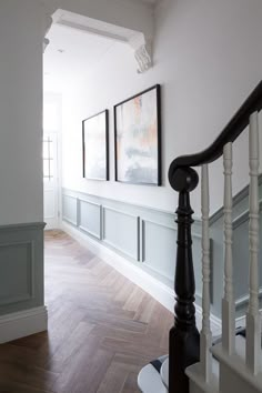 an empty hallway with wooden floors and white walls, framed pictures on the wall above the banister