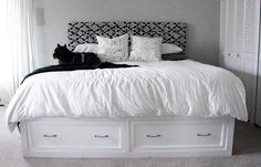 a white bed with two drawers underneath it and a black cat laying on the pillow