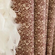 white feathers are hanging from the side of a brown and white wallpapered curtain