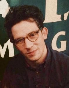 a man with glasses is sitting in front of a sign