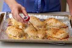 a person using a thermometer to check food on a baking sheet with chicken