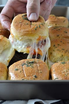 someone is dipping cheese on top of mini sandwiches in a baking pan with other buns