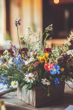 an arrangement of wildflowers and other flowers in a wooden vase on a table