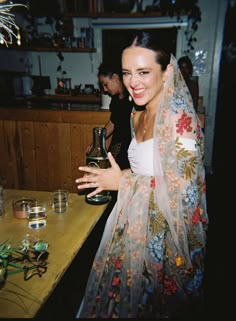 a woman wearing a veil holding a bottle in her right hand and smiling at the camera