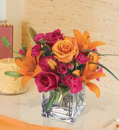 a vase filled with orange and pink flowers on top of a table next to a candle