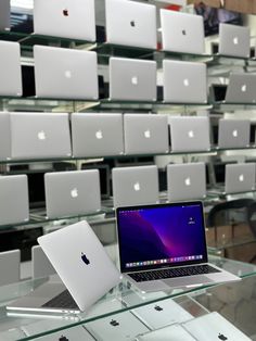 an apple laptop sitting on top of a glass table in front of rows of white macbooks